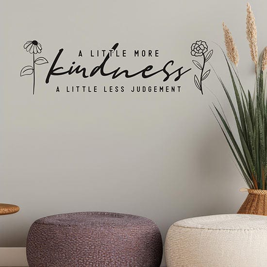 Adesivo murale motivazionale con la frase 'A Little More Kindness, A Little Less Judgement' e dettagli floreali minimalisti, ideale per decorare soggiorni, camere da letto o uffici con eleganza e positività.