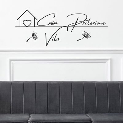 Scritta adesiva decorativa da muro con le parole "Casa, Protezione, Vita" in calligrafia moderna, applicata sopra un divano grigio su parete bianca con cornici eleganti.