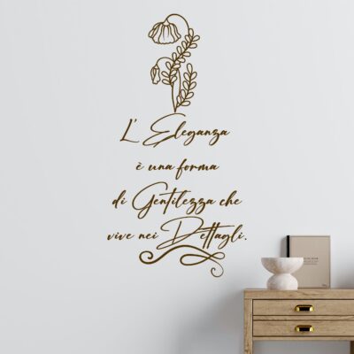 Adesivo murale decorativo su parete bianca con frase elegante in calligrafia marrone e fiore stilizzato. Citazione su eleganza e gentilezza, perfetta per soggiorno moderno o classico.