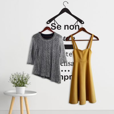 Appendiabiti adesivi con scritte nere e pomelli in metallo utilizzati per appendere abiti su parete bianca.