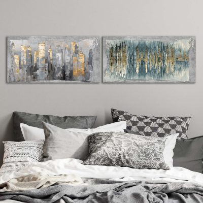 Quadri astratti camera da letto appesi sopra letto matrimoniale con cuscini in stile neutro.